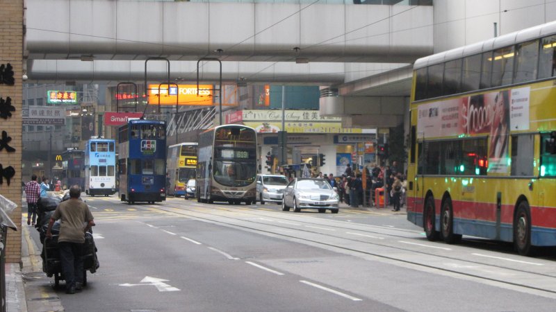 Dwupiętrowe tramwaje i autobusy, po lewej dziadek z taczką